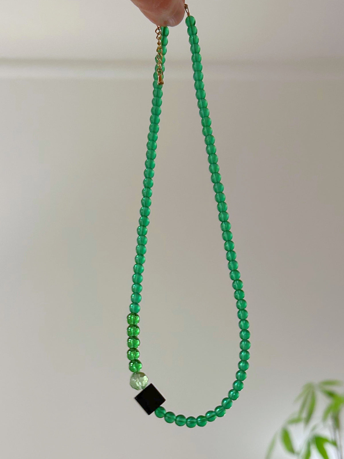 Collier ras du cou en perles de verre blanc, vert et noir suspendu, détail de la perle cube noire