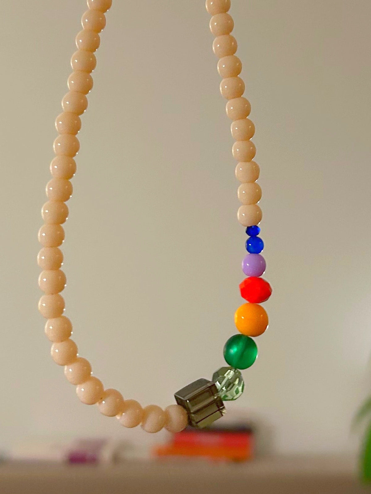 Gros plan du collier ras du cou en perles de verre beige, perles arc-en-ciel au centre
