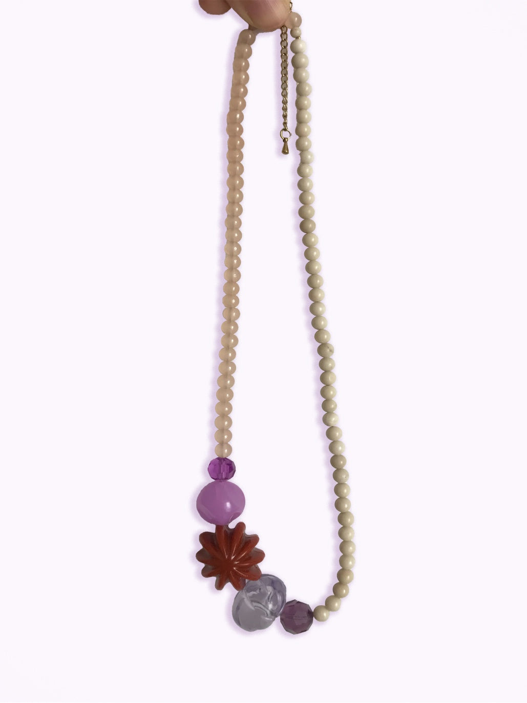 Détail du collier en perles beiges, violettes et perle fleur marron, sur fond blanc