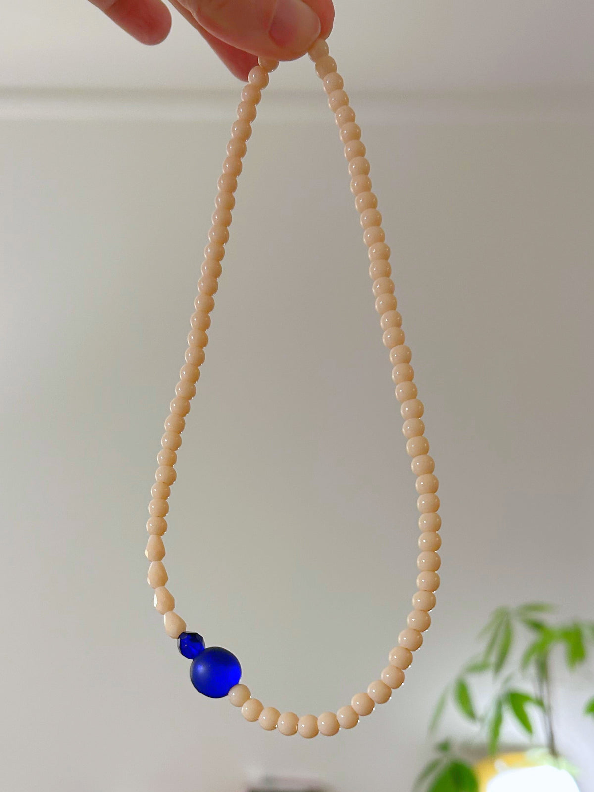 Gros plan du collier ras du cou en perles de verre blanc cassé, perle bleue au centre