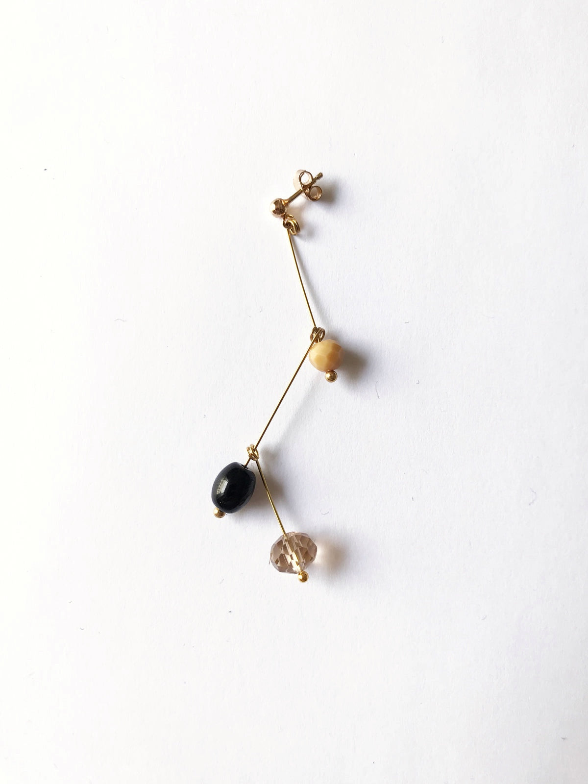 Petite boucle d'oreille mobile n°2, perles beige, noire et transparente, sur fond blanc