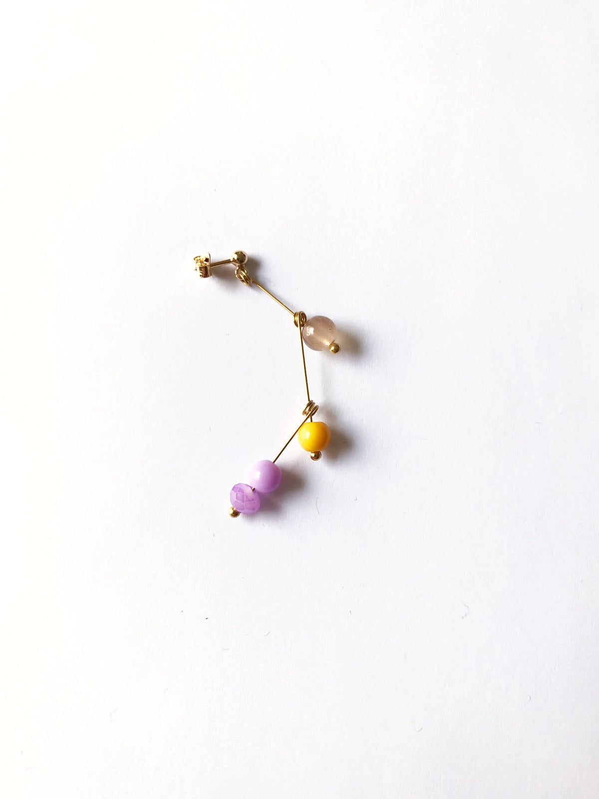 Petite boucle d'oreille mobile n°3, perles beige, jaune et mauve, sur fond blanc