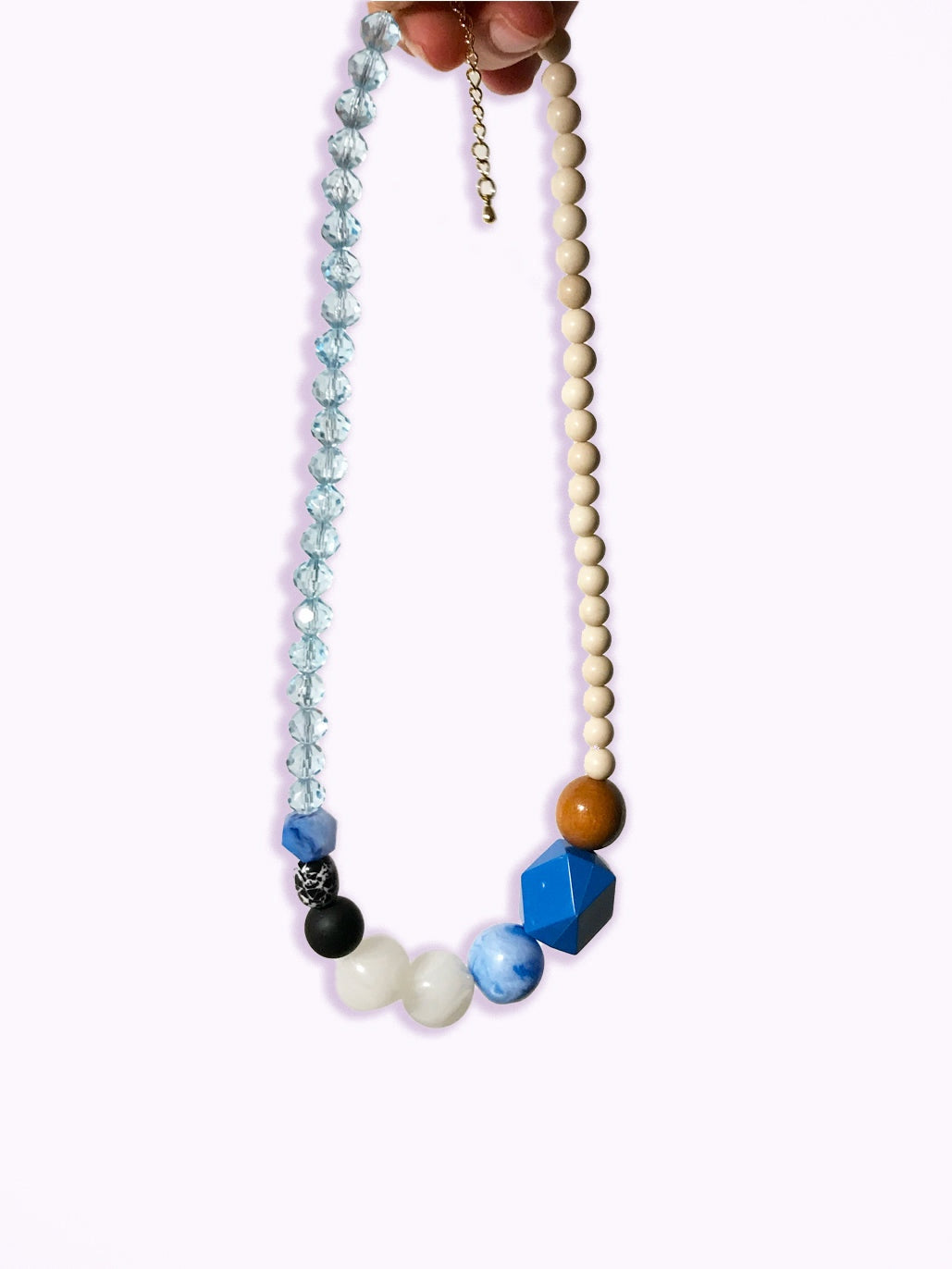 Détail du collier en perles bleu cristal, blanches, noire et bois, sur fond blanc