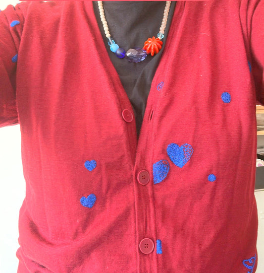 Collier en grosses perles marron et bleues porté sur un gilet rouge