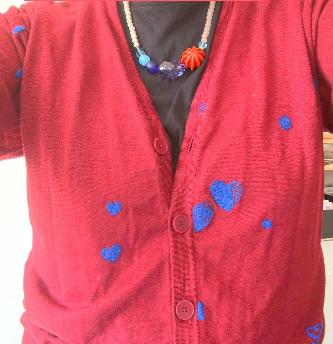 Collier en grosses perles marron et bleues porté sur un gilet rouge