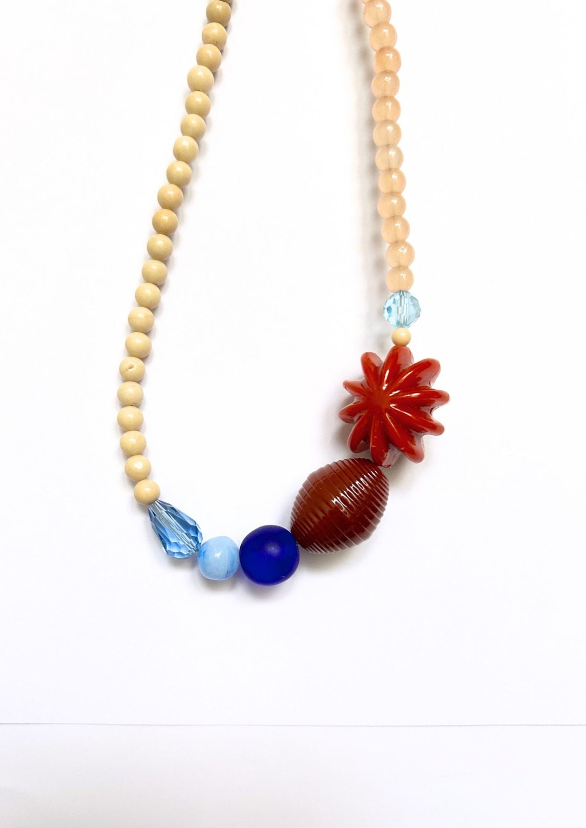 Collier de perles beige, bleu et fleur rouge : gros plan sur la fleur rouge, la perle marron rayée et les perles bleues