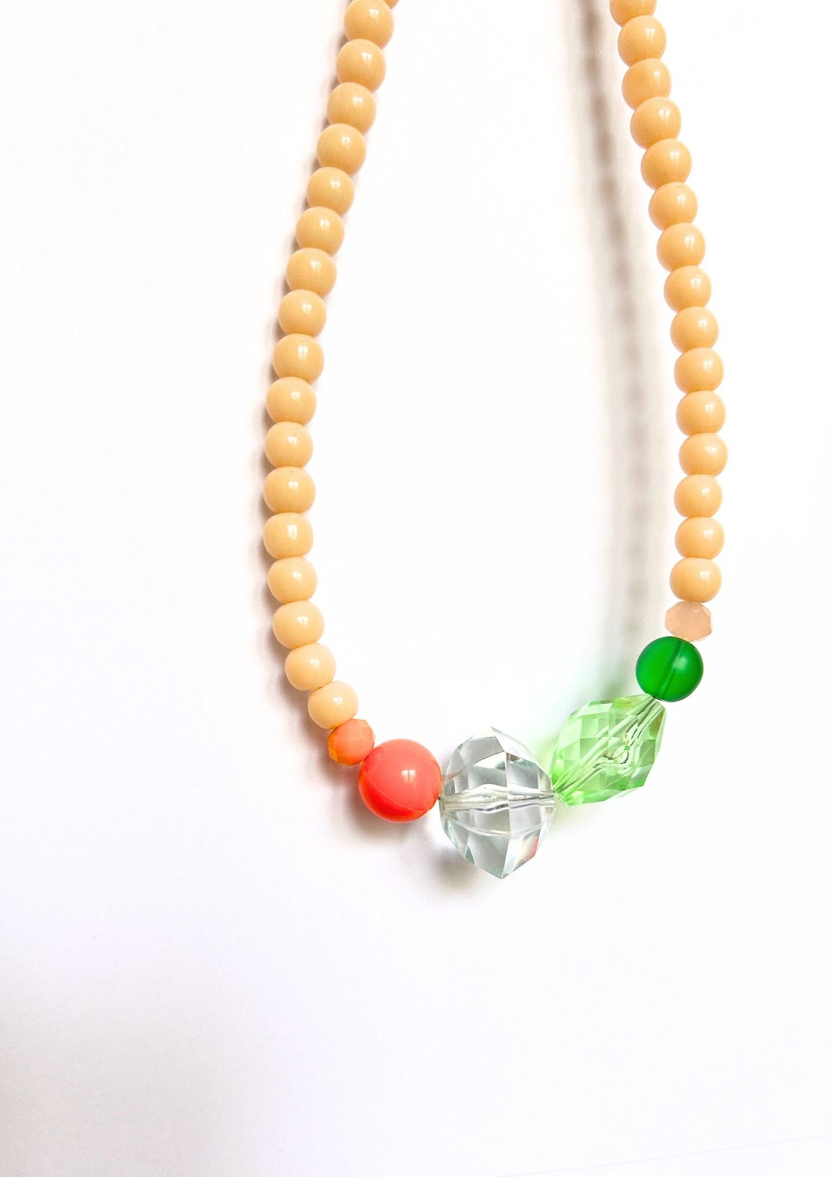 Collier de perles beige, vert et corail : gros plan sur la perle corail, le cristal transparent et les perles vertes