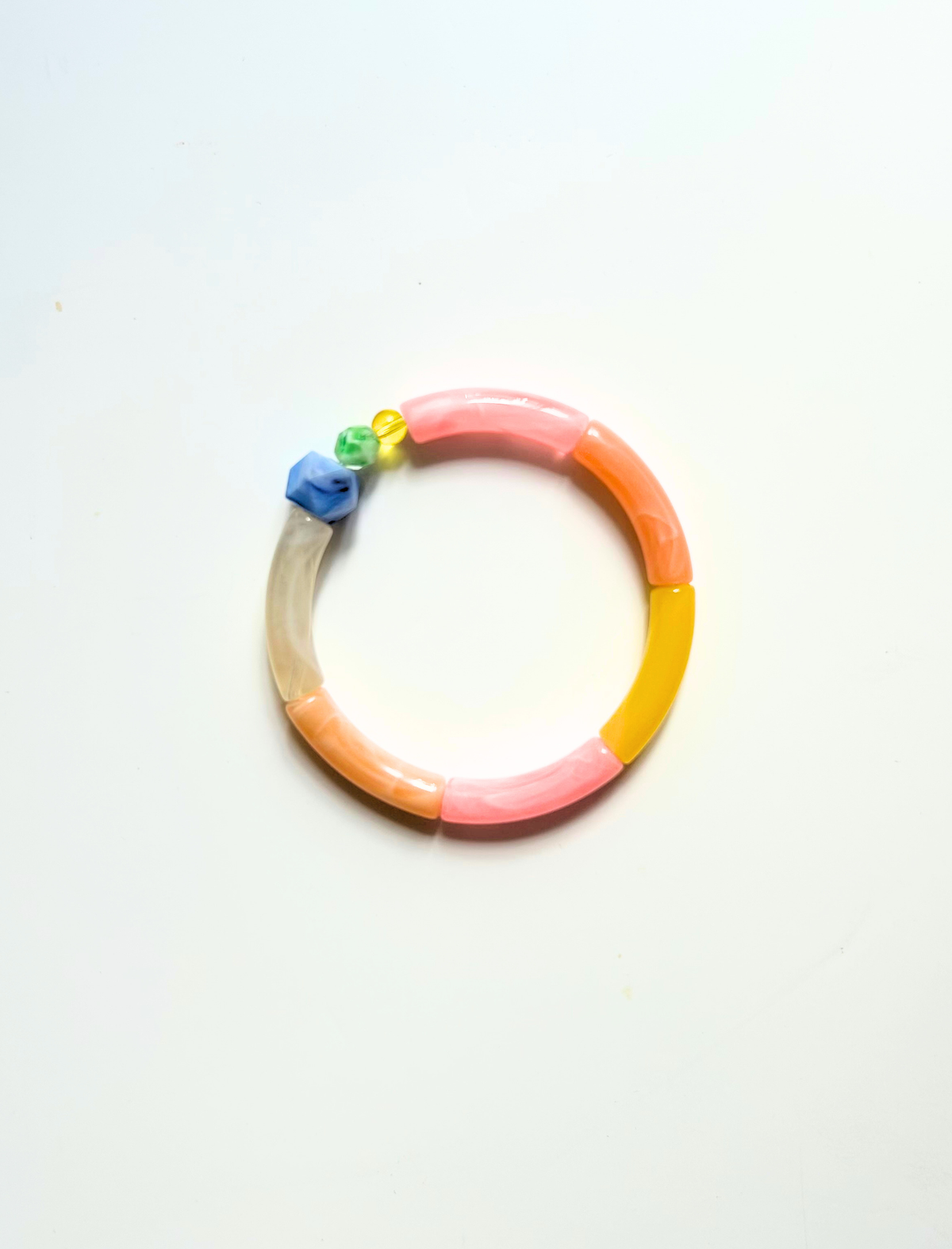Petit bracelet pièce unique n°1 en perles tubes rose, pêche, jaune et taupe, perle bleue facettée et perles verte et jaune, posé sur fond blanc