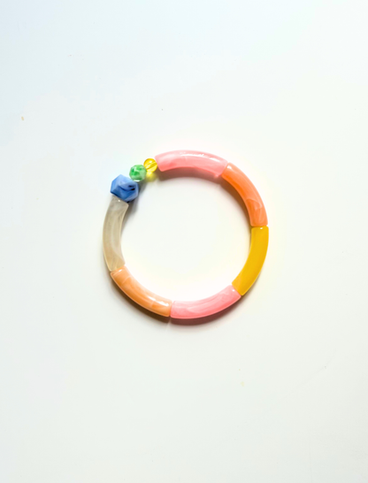 Petit bracelet pièce unique n°1 en perles tubes rose, pêche, jaune et taupe, perle bleue facettée et perles verte et jaune, posé sur fond blanc