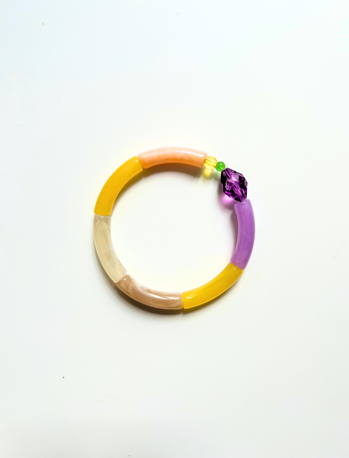 Petit bracelet pièce unique n°11 en perles tubes pêche, jaune, crème, taupe et lavande, perle violette facettée, perles jaune et verte, posé sur fond blanc