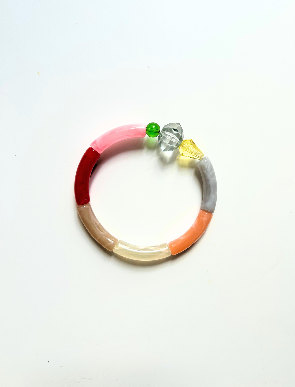 Petit bracelet pièce unique n°2 en perles tubes rose, rouge, taupe, crème, pêche et gris, perle transparente facettée, perles verte et jaune, posé sur fond blanc