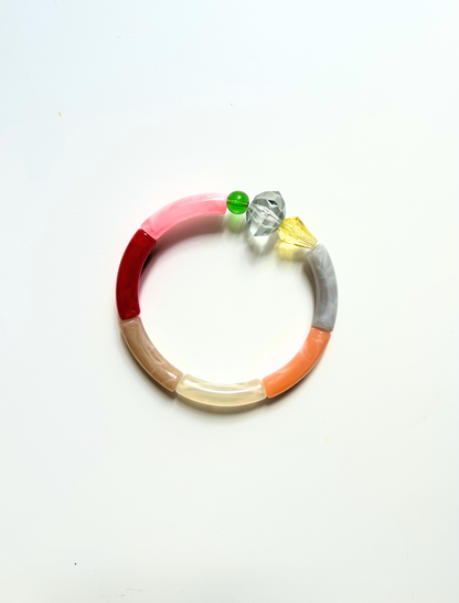 Petit bracelet pièce unique n°2 en perles tubes rose, rouge, taupe, crème, pêche et gris, perle transparente facettée, perles verte et jaune, posé sur fond blanc