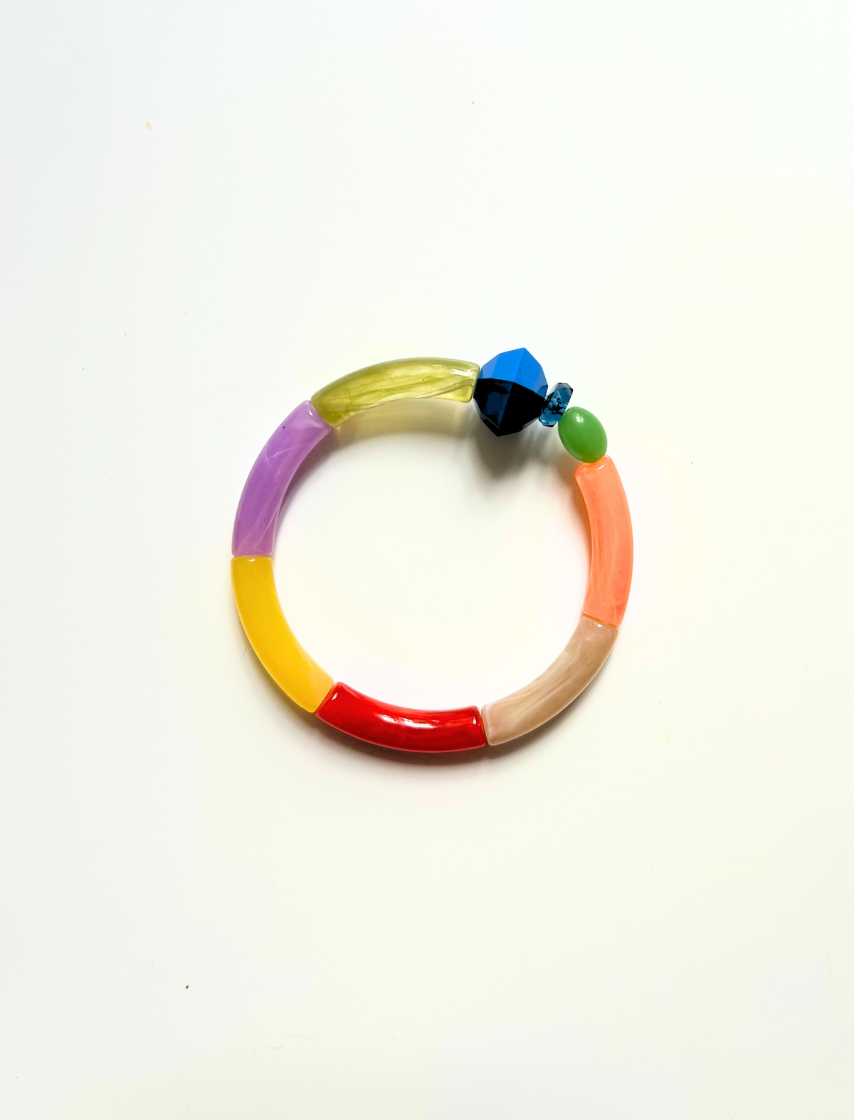 Petit bracelet pièce unique n°8 en perles tubes vert anis, lavande, jaune, rouge, taupe et corail, perle bleue et noire facettée, perle verte ovale, posé sur fond blanc