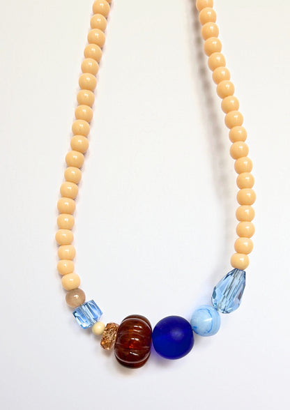 Détail du collier Maison Chouquette : perle côtelée marron ambré, grosse perle bleu roi givrée, perle bleu ciel marbrée et gouttes bleu glacier facettées