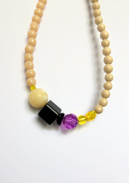 Détail du collier Maison Chouquette : grosse perle crème, cube noir brillant, facette violette, perle et goutte jaunes facettées