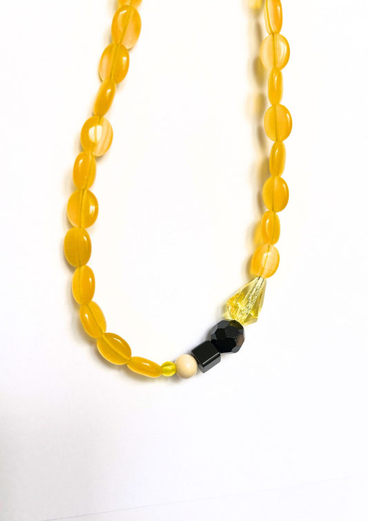Collier de perles jaune et noir : gros plan sur les perles ovales jaunes, la facette noire et le cristal jaune