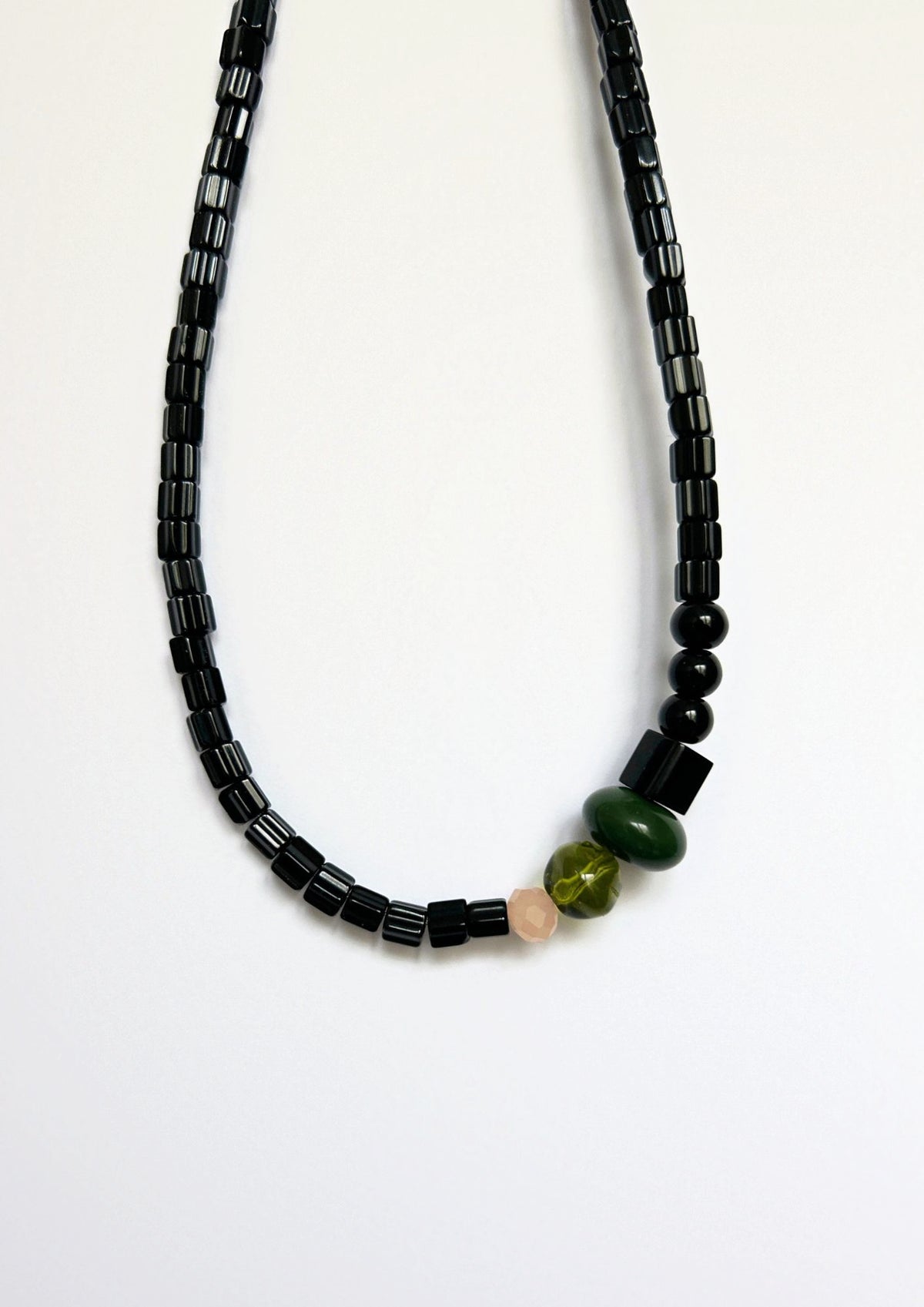 Collier de perles noir, vert et beige : gros plan sur les perles tubes noires et les perles vertes au centre