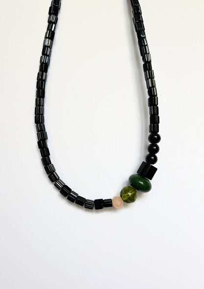 Collier de perles noir, vert et beige : gros plan sur les perles tubes noires et les perles vertes au centre